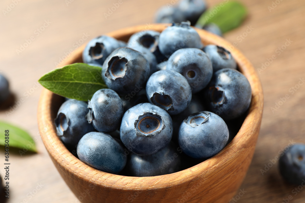 Bowl of tasty fresh blueberries with green leaves on table, closeup Bowl of tasty fresh blueberries with green leaves on table, closeup
