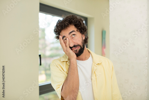 young crazy bearded man feeling bored, frustrated and sleepy after a tiresome, dull and tedious task, holding face with hand photo