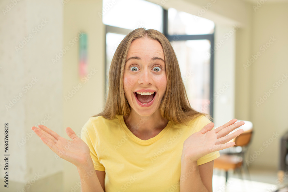 pretty blond woman feeling happy, excited, surprised or shocked, smiling and astonished at something unbelievable