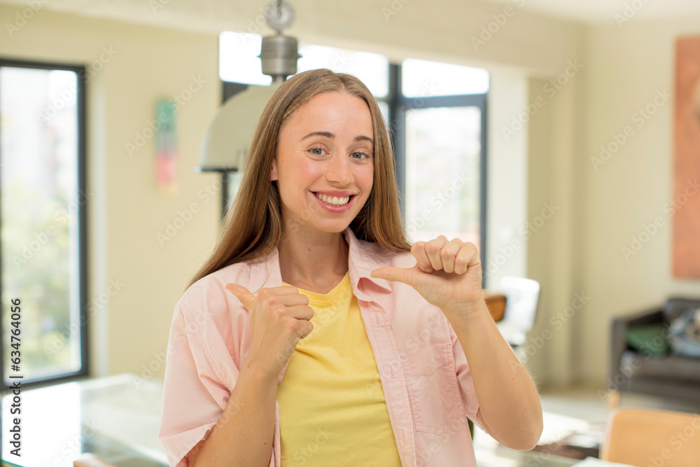 pretty blond woman smiling cheerfully and casually pointing to copy space on the side, feeling happy and satisfied