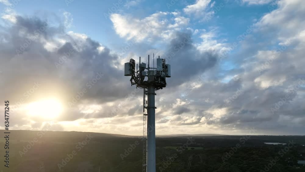 Cell tower with antennas at top with dramatic sky at sunset. Drone shot rising up with camera tracking the antenna array.