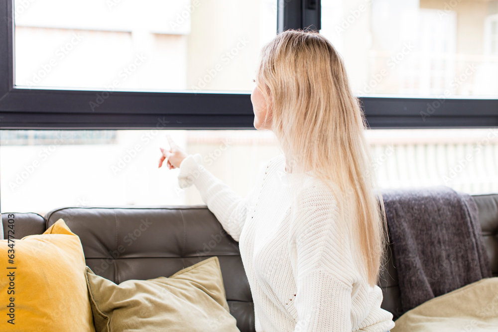 young pretty woman standing and pointing to object on copy space, rear view sitting on a couch young pretty woman standing and pointing to object on copy space, rear view sitting on a couch