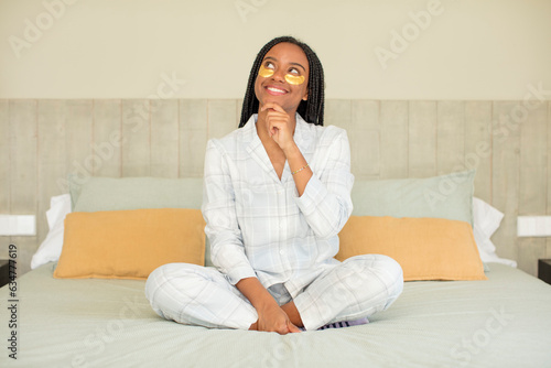 black afro woman smiling with a happy, confident expression with hand on chin. rest and nightwear concept