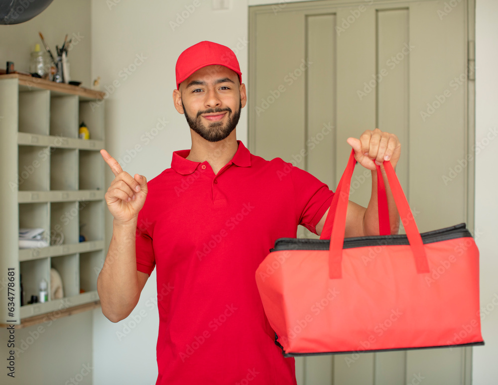 young adult man smiling cheerfully, feeling happy and pointing to the side. pizza deliveryman concept young adult man smiling cheerfully, feeling happy and pointing to the side. pizza deliveryman concept