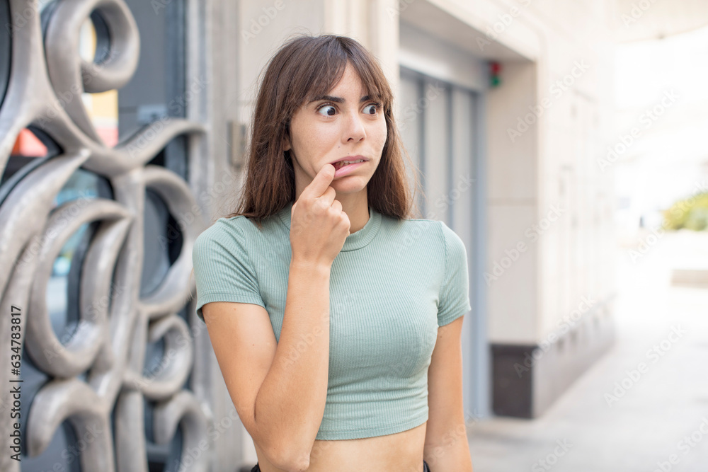 pretty young woman with surprised, nervous, worried or frightened look, looking to the side towards copy space pretty young woman with surprised, nervous, worried or frightened look, looking to the side towards copy space