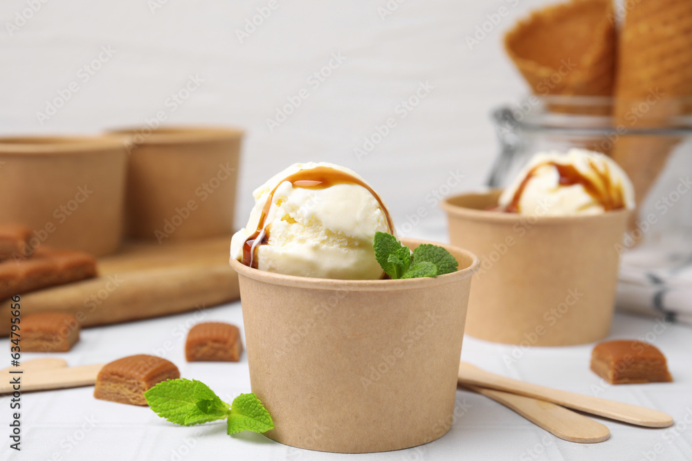 Scoops of ice cream with caramel sauce, mint leaves and candies on white tiled table, closeup Scoops of ice cream with caramel sauce, mint leaves and candies on white tiled table, closeup
