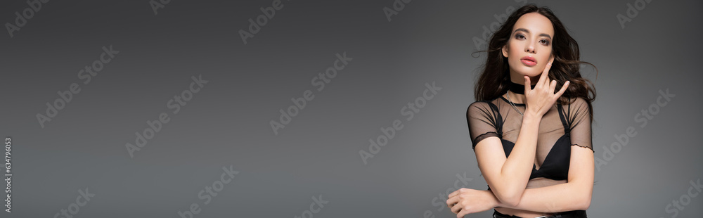 Attractive asian woman in mesh top and necklaces looking at camera isolated on grey, banner Attractive asian woman in mesh top and necklaces looking at camera isolated on grey, banner