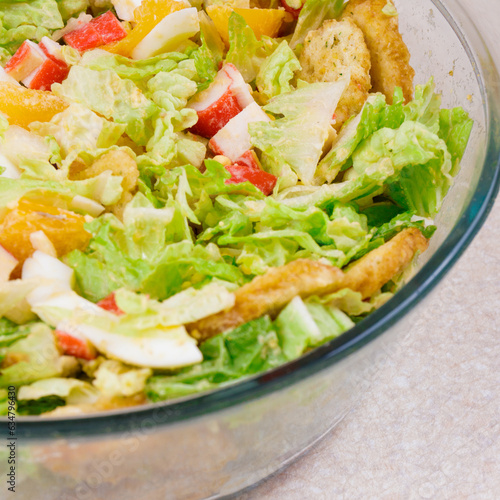 Salad with crab sticks, tomatoes, napa cabbage, eggs, lettuce and croutons in glass bowl. 