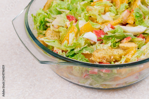 Salad with crab sticks, tomatoes, napa cabbage, eggs, lettuce and croutons in glass bowl. 