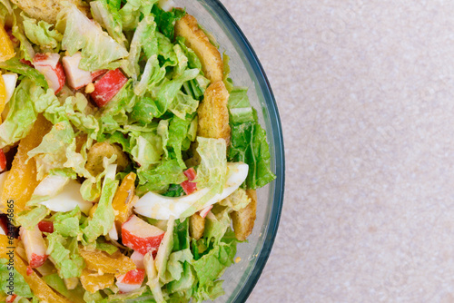 Salad with crab sticks, tomatoes, napa cabbage, eggs, lettuce and croutons in glass bowl. Top view.