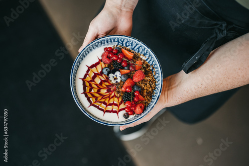 Person holding healthy breakfast acai bowl with red fruit and granola photo