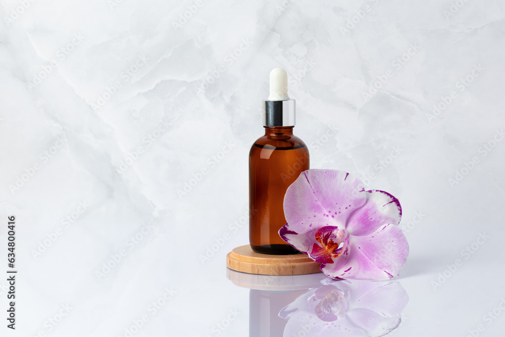 Brown glass bottle on wooden podium and pink orchid flower close-up. Aromatic massage oil on gray marble background with reflection. Natural organic spa cosmetics, skin care concept. Beauty product. Brown glass bottle on wooden podium and pink orchid flower close-up. Aromatic massage oil on gray marble background with reflection. Natural organic spa cosmetics, skin care concept. Beauty product.