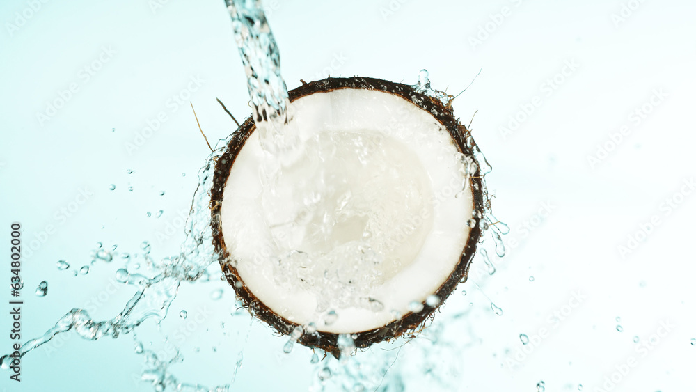 Cracked coconut with splashing water on blue background Cracked coconut with splashing water on blue background
