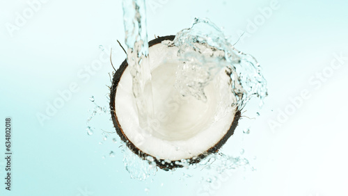 Cracked coconut with splashing water on blue background