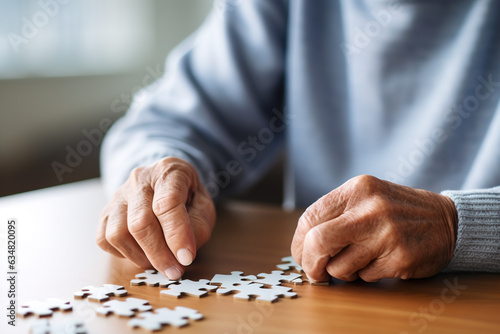 Close-up of senior man putting jigsaw puzzle piece on wooden table. The concept of age-related changes in mental health.