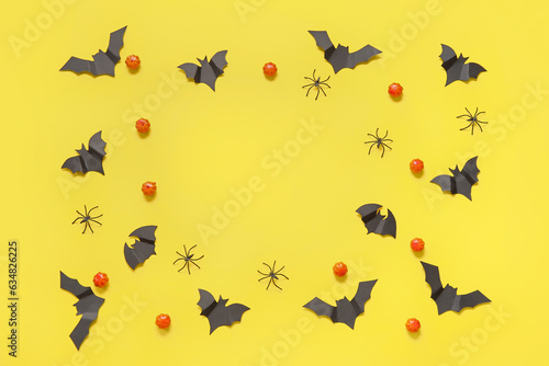 Frame made of pumpkins, paper bats and spiders on yellow background. Halloween celebration concept