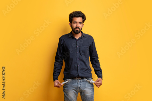 Poverty Concept. Portrait Of Upset Young Indian Man Showing His Empty Pockets