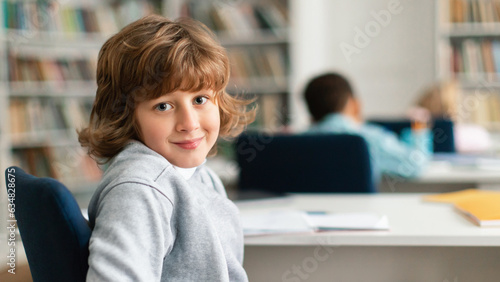 Happy caucasian smart primary schoolboy sitting in classroom, looking and smiling at camera, panorama, copy space