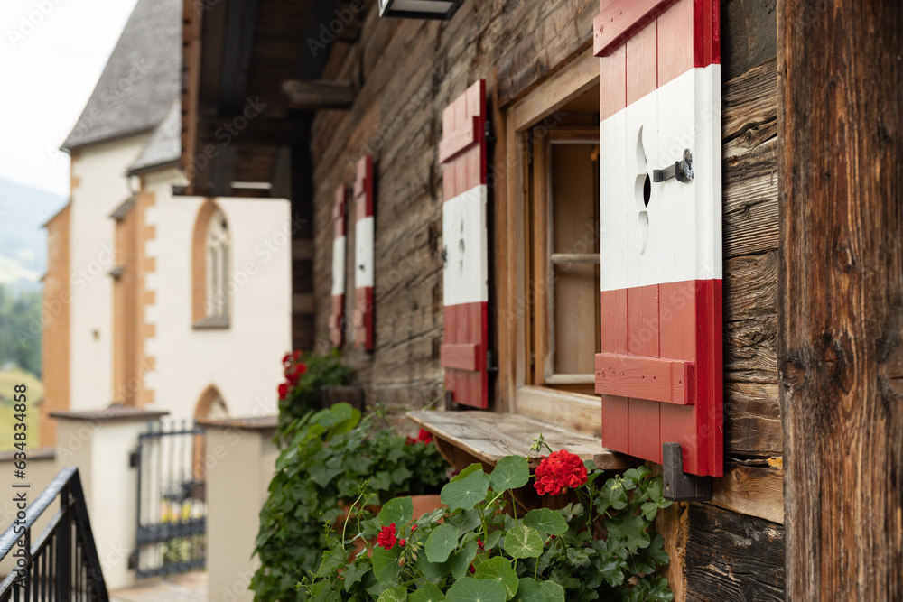 Beautiful decoration of the fasade of a wooden house with painted shutters and flowers, Austria Beautiful decoration of the fasade of a wooden house with painted shutters and flowers, Austria