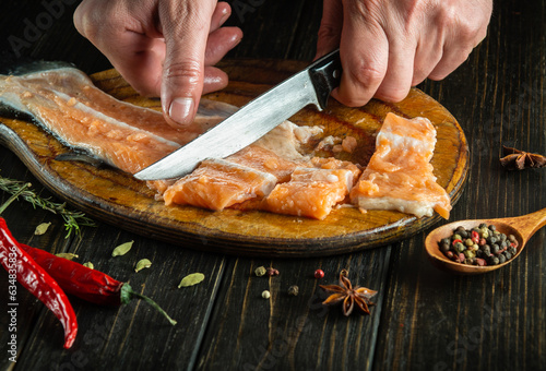 A butcher cuts raw salmon fish on a kitchen cutting board with a knife. Delicious lunch of red fish for a restaurant or hotel by the hands of a chef