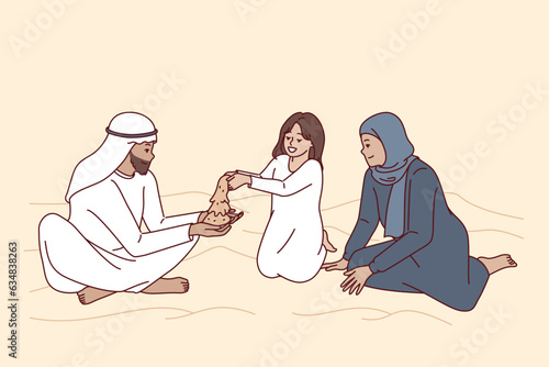 Arab family sits in desert with dunes, playing with daughter with sand and enjoying joint weekend. Happy family from arab emirates or qatar dressed in ethnic clothes, for concept oriental culture