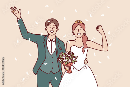 Wedding bride and groom with bouquet waving hand during festive marriage ceremony. Happy man and woman are proud of creation of new family and greet relatives or friends attended wedding celebration