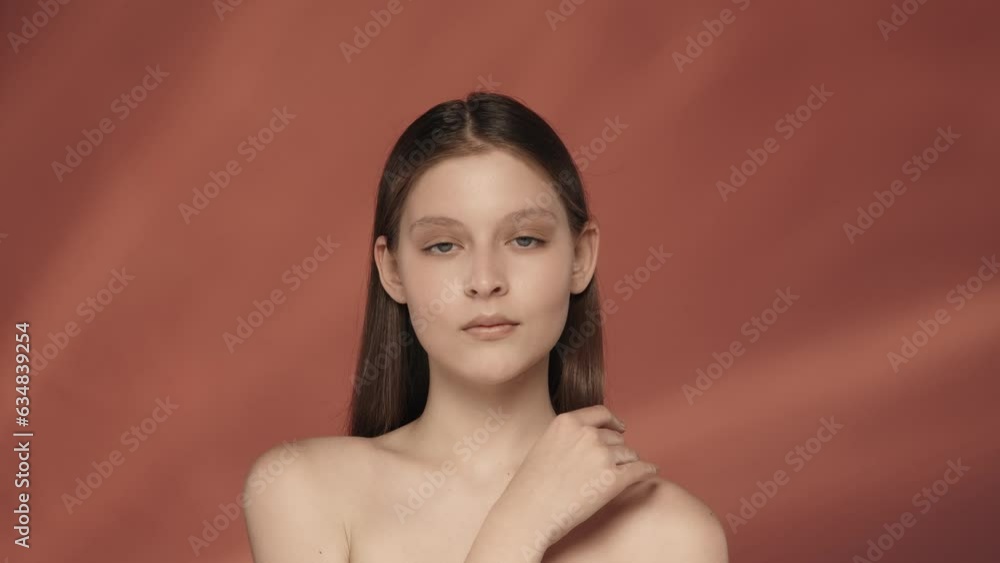 The young woman enjoys her smooth, clean silky skin, runs her hand over her bare shoulders and across her face. Portrait of a seminude smiling woman in the studio on a red background. Slow motion. The young woman enjoys her smooth, clean silky skin, runs her hand over her bare shoulders and across her face. Portrait of a seminude smiling woman in the studio on a red background. Slow motion.