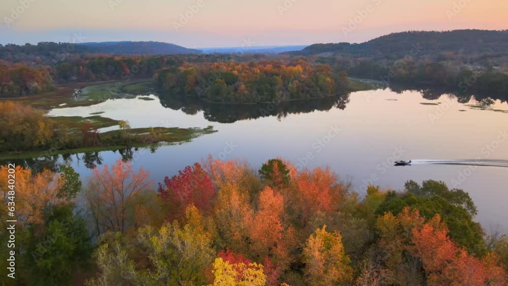 Boat motors over glassy lake reflection during fall with autumn colored country leaves aerial drone shot Boat motors over glassy lake reflection during fall with autumn colored country leaves aerial drone shot