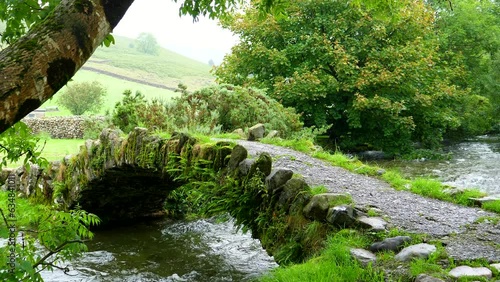 Old mossy lovely little stone arch bridge over mountain stream in summer Lake District, England, United Kingdom.
