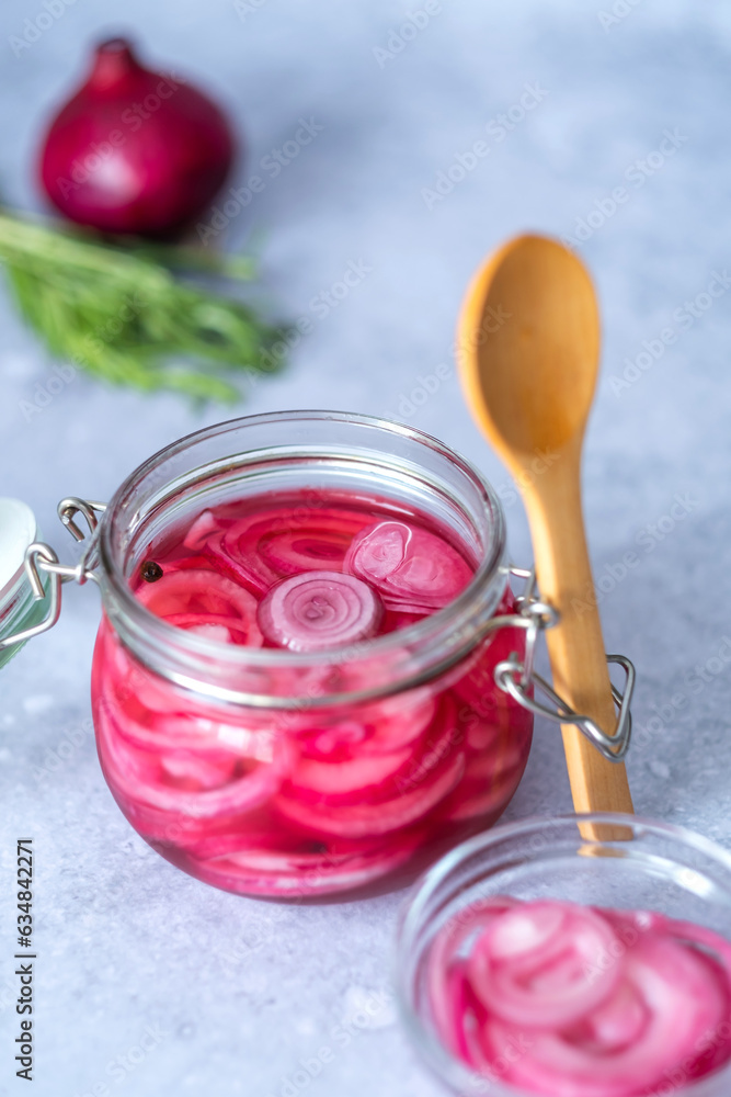 Pickled red onions in glass jar with a wooden spoon on a gray background. Appetizer, condiment or topping. Healthy fermented food. Pickled red onions in glass jar with a wooden spoon on a gray background. Appetizer, condiment or topping. Healthy fermented food.