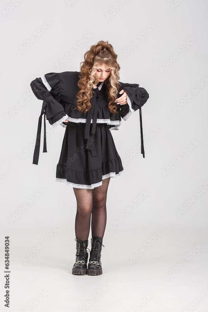 young girl in black school dress poses as doll on white background in studio young girl in black school dress poses as doll on white background in studio