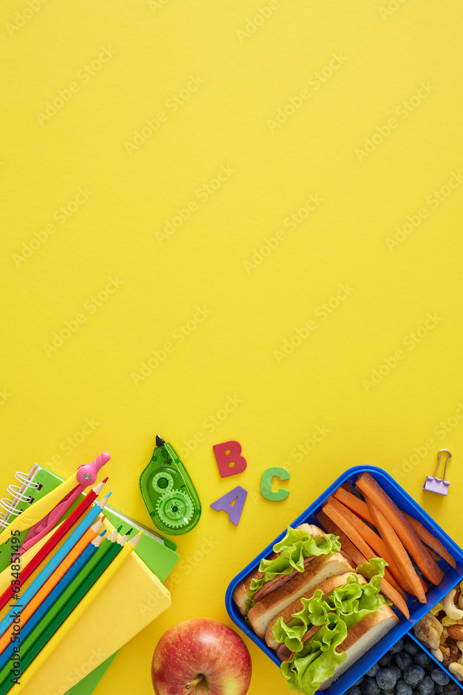 Obraz premium Delicious and nutritious school break. Top view vertical photo of educational stationery, sandwiches and organic treats on yellow background with blank space for promo or message