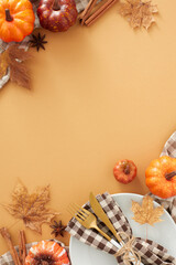 Autumnal charm brought to the table. Top view vertical shot of plate, cutlery, napkin, tablecloth, pumpkins, cinnamon sticks, anise, dry leaves on brown background with space for promo or text