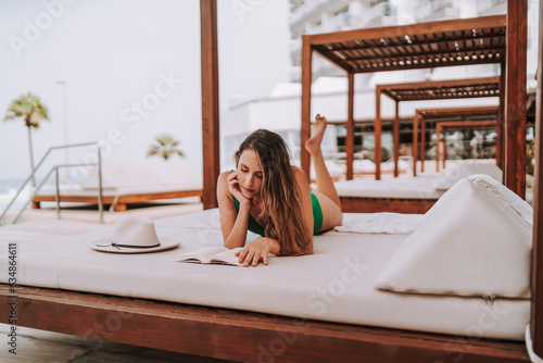 Chica joven delgada en cama balinesa descansando y leyendo tranquilamente  photo