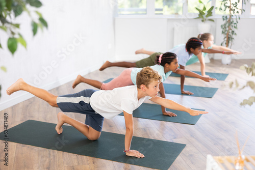Concentrated children performing asana Dandyamana Brahmanaasana during group yoga course in fitness studio