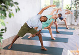 In fitness studio with group of friends, African boy children perform elongated lateral angle, Parshvakonasana. Male teen participates in yoga practice. Concept of active lifestyle of young generation