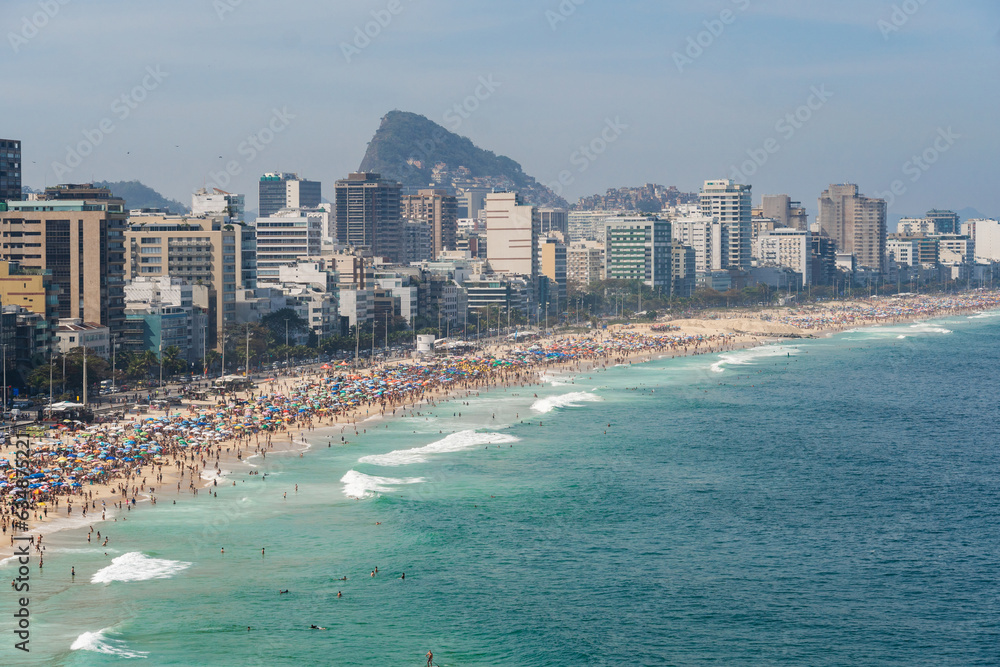 Leblon and Ipanema beach in Rio de Janeiro, Brazil. Sunny day with blue sky and many people on the beach. Plenty of umbrellas on the sand. Weekend. Turquoise and clear sea