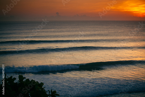 Viewed from above  a wave rolls gracefully  its crest illuminated by the sun s amber descent  casting a golden silhouette against the deepening hues of the horizon.