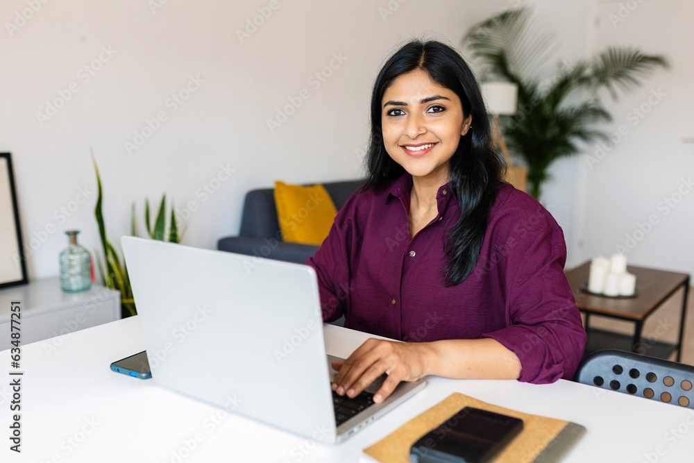 Portrait of cheerful indian business woman smile at camera using laptop at home. Entrepreneur and freelancer people concept. Portrait of cheerful indian business woman smile at camera using laptop at home. Entrepreneur and freelancer people concept.