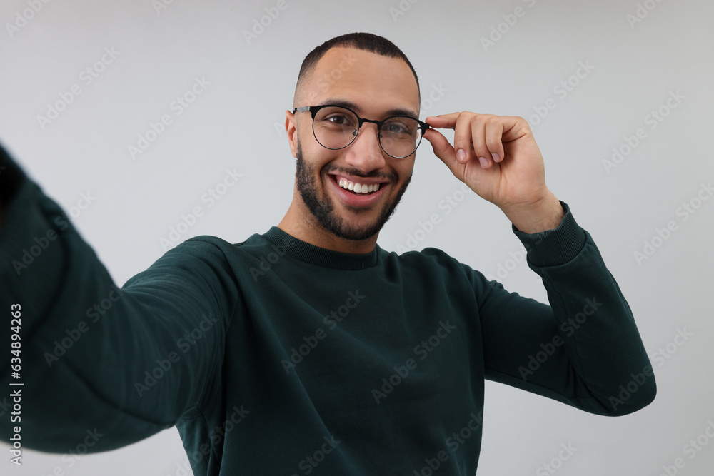 Smiling young man taking selfie on grey background Smiling young man taking selfie on grey background