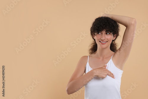 Smiling young woman doing breast self-examination on light brown background. Space for text