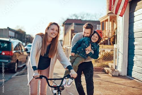 Young family walking and riding a bike on the sidewalk in the suburbs of the city © Geber86