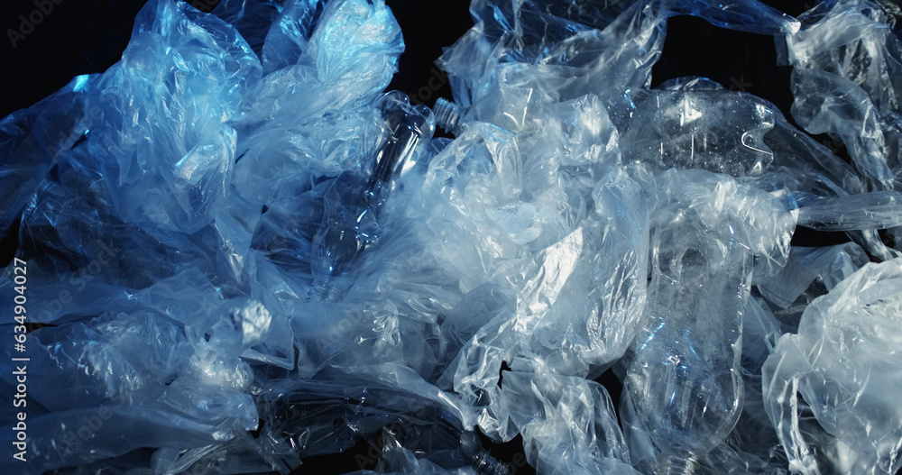 Waste management. Plastic recycling. Used wet empty cellophane polyethylene transparent bags crushed bottles garbage rubbish on dark background. Waste management. Plastic recycling. Used wet empty cellophane polyethylene transparent bags crushed bottles garbage rubbish on dark background.
