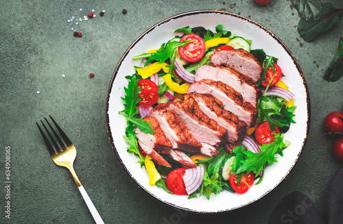 Salad with grilled duck breast slices and cherry tomatoes, cucumber, paprika, red onion, lettuce and arugula on green table background, top view