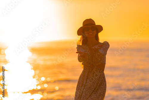 Young beautiful woman at straw hat on the beach at sunset