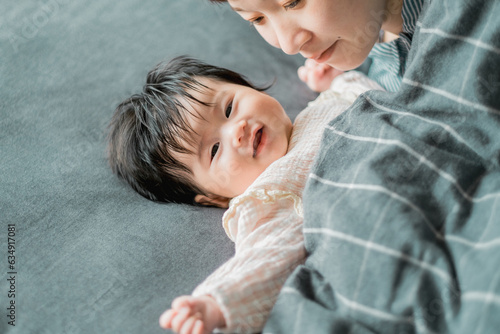 春の昼過ぎ、布団で寝る日本人の黒髪の子どもと見つめる母親の親子