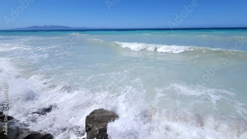 Panoramic shot of shoreline with cliffs splashed by white waves and blue turquoise sea background in Albania