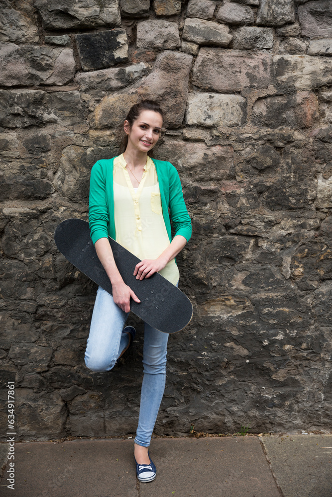 Happy young woman holding skateboard on city street. Happy young woman holding skateboard on city street.