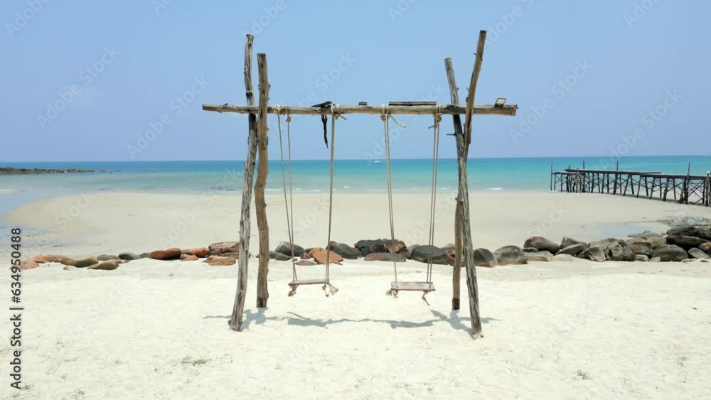 View of two swings on a tropical paradise beach with white sand and turquoise water in the background. View of two swings on a tropical paradise beach with white sand and turquoise water in the background.