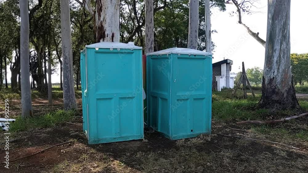 travelling out of gender-neutral aqua green blue portable bathrooms, in a park with forest travelling out of gender-neutral aqua green blue portable bathrooms, in a park with forest